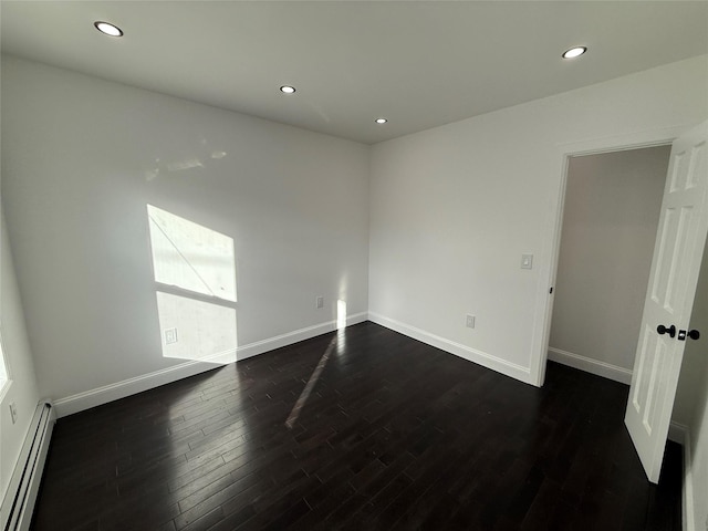 empty room featuring baseboard heating and dark wood-type flooring