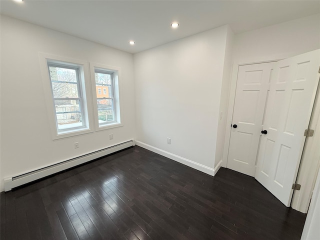 empty room with dark hardwood / wood-style flooring and a baseboard heating unit