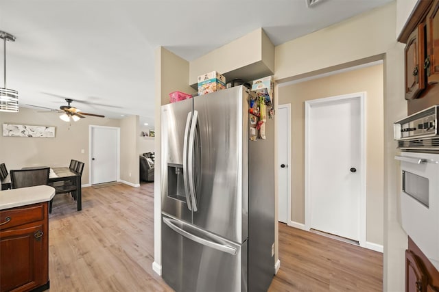 kitchen featuring light wood-type flooring, white oven, ceiling fan, stainless steel fridge with ice dispenser, and hanging light fixtures