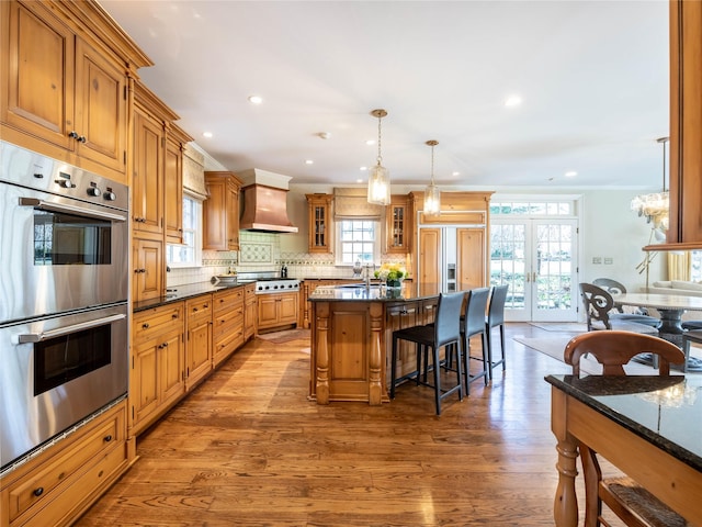 kitchen with stainless steel appliances, a kitchen breakfast bar, hanging light fixtures, wall chimney exhaust hood, and a center island