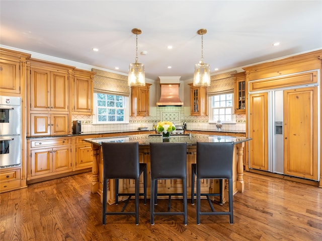 kitchen with a center island, custom exhaust hood, plenty of natural light, double oven, and paneled refrigerator