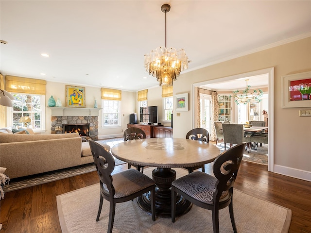 dining room featuring a chandelier, dark hardwood / wood-style flooring, ornamental molding, and a stone fireplace