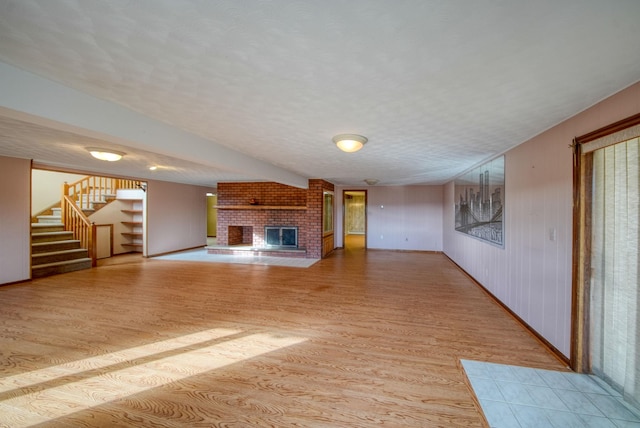 unfurnished living room featuring a brick fireplace, a textured ceiling, wood walls, and light hardwood / wood-style flooring