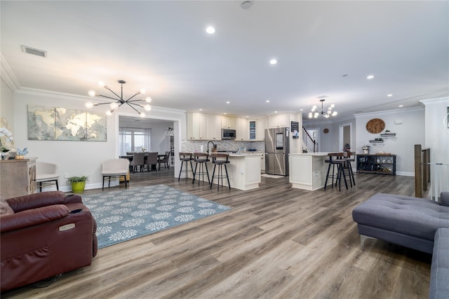 living room with sink, hardwood / wood-style flooring, a chandelier, and ornamental molding