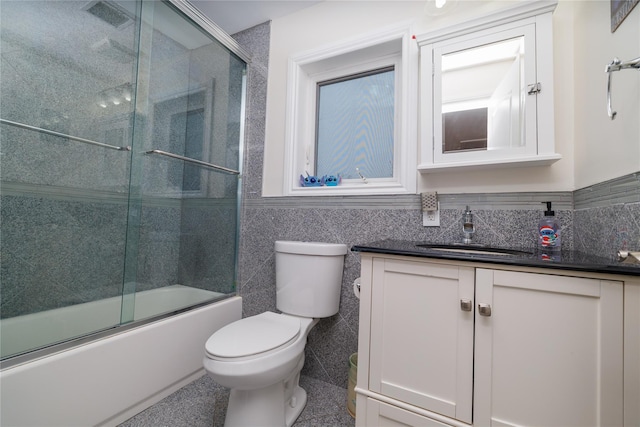 full bathroom with bath / shower combo with glass door, toilet, vanity, and tile walls