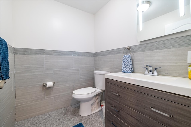 bathroom featuring toilet, vanity, and tile walls