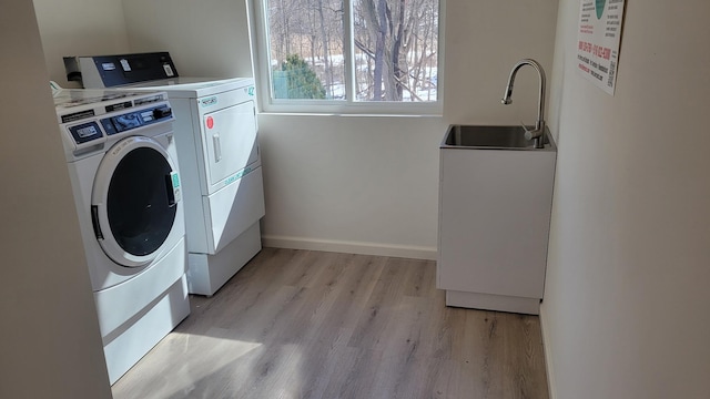 shared laundry area featuring light wood-type flooring, washer and dryer, a sink, and baseboards