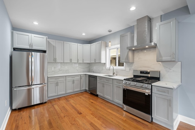 kitchen featuring sink, stainless steel appliances, wall chimney range hood, decorative light fixtures, and light wood-type flooring