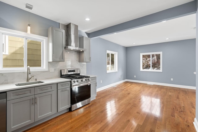 kitchen with gray cabinetry, wall chimney range hood, sink, beamed ceiling, and stainless steel appliances