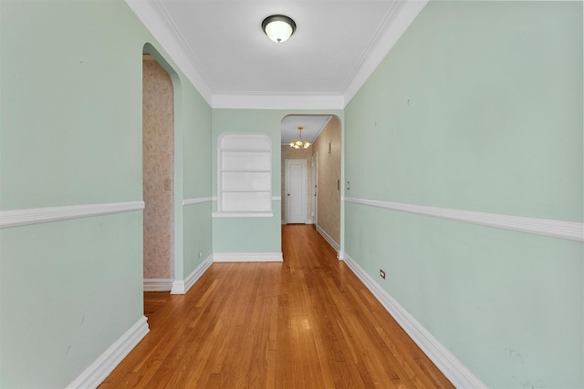 hall with light wood-type flooring, ornamental molding, and an inviting chandelier