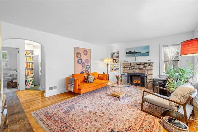 living room featuring a stone fireplace, built in features, wood-type flooring, and a wealth of natural light