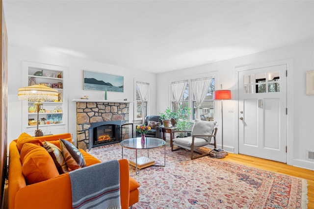 living room featuring built in shelves, a stone fireplace, and hardwood / wood-style floors