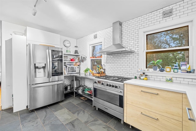 kitchen featuring light brown cabinetry, track lighting, tasteful backsplash, wall chimney exhaust hood, and stainless steel appliances