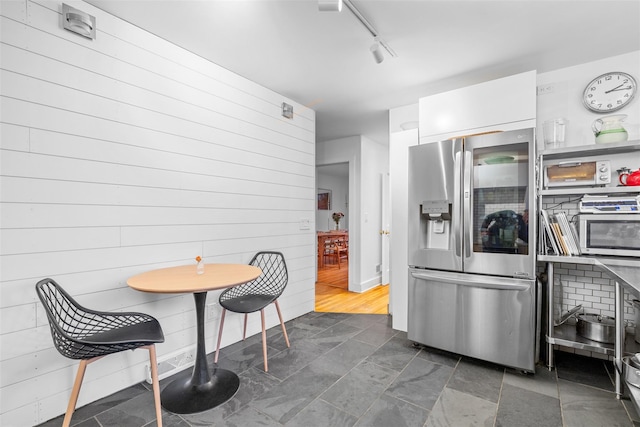 kitchen featuring white cabinets, stainless steel fridge with ice dispenser, rail lighting, and wood walls