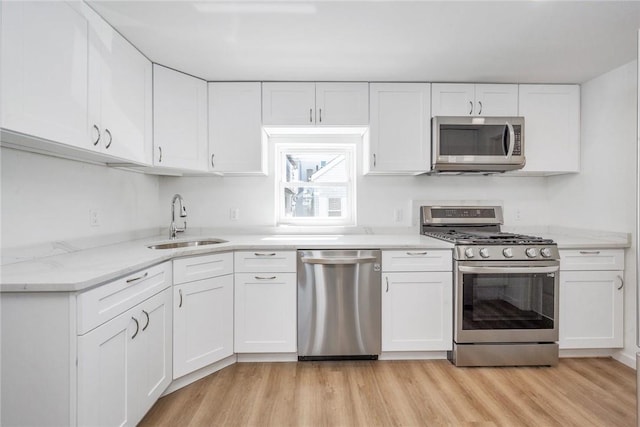 kitchen with appliances with stainless steel finishes, light stone counters, sink, light hardwood / wood-style flooring, and white cabinetry