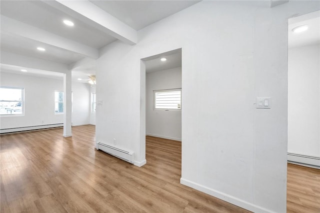 empty room with beamed ceiling, light hardwood / wood-style floors, and a baseboard heating unit