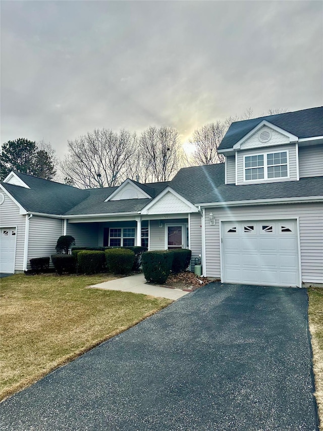 view of front of home with an attached garage, aphalt driveway, roof with shingles, and a front yard