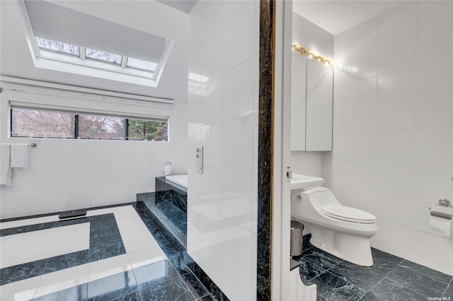 bathroom with a washtub, a skylight, toilet, and tile walls