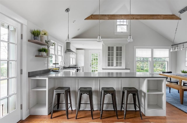 kitchen with pendant lighting, beam ceiling, wall chimney range hood, and sink