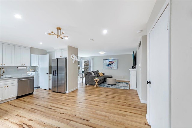 kitchen with appliances with stainless steel finishes, backsplash, sink, light hardwood / wood-style flooring, and white cabinets