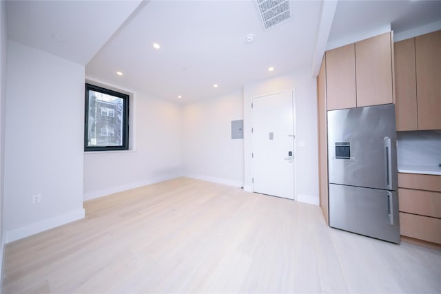 kitchen with electric panel, stainless steel fridge with ice dispenser, light brown cabinetry, and light wood-type flooring