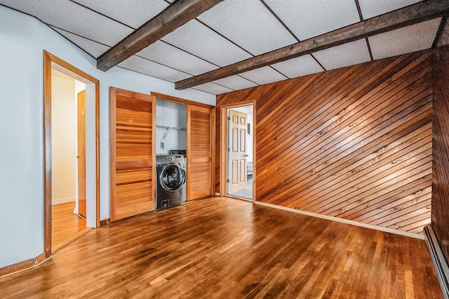 interior space with a drop ceiling, wood walls, hardwood / wood-style floors, washer / dryer, and a closet