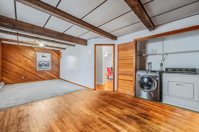 clothes washing area featuring wooden walls, ceiling fan, washer and dryer, and hardwood / wood-style flooring