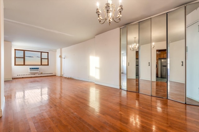 unfurnished room with hardwood / wood-style flooring, a notable chandelier, and a baseboard radiator