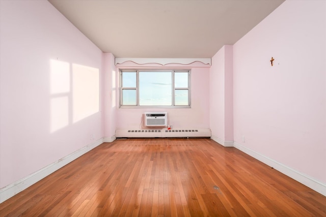 spare room with an AC wall unit, light hardwood / wood-style flooring, and a baseboard heating unit