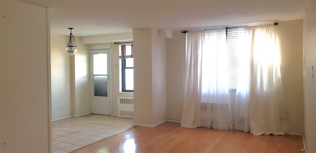 empty room featuring light hardwood / wood-style floors, a healthy amount of sunlight, and radiator heating unit