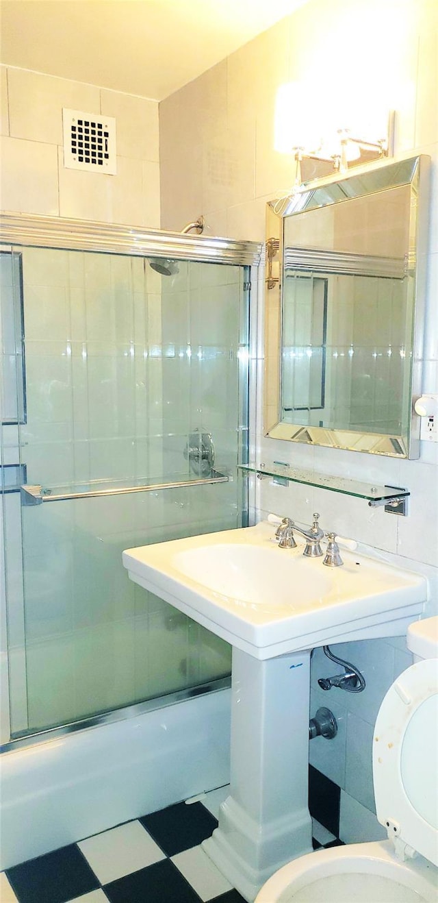 bathroom with toilet, tile walls, and bath / shower combo with glass door