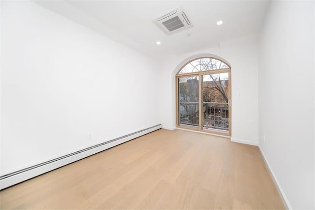 unfurnished room with baseboard heating and light wood-type flooring