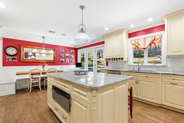 kitchen with wainscoting, a kitchen island, light stone countertops, pendant lighting, and a sink