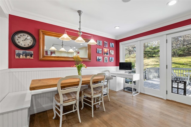 dining area with light wood-style flooring, breakfast area, crown molding, and wainscoting