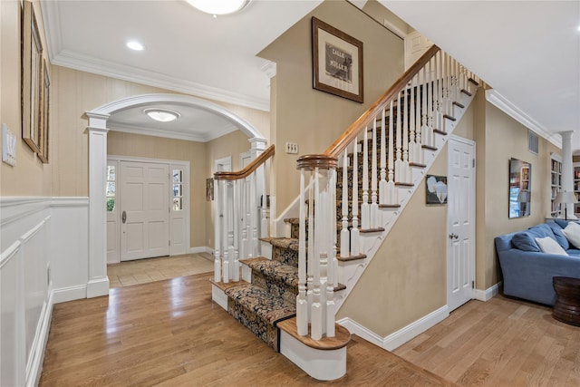 entrance foyer featuring arched walkways, light wood finished floors, wainscoting, and crown molding