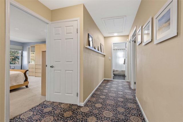 hall with attic access, light carpet, and baseboards