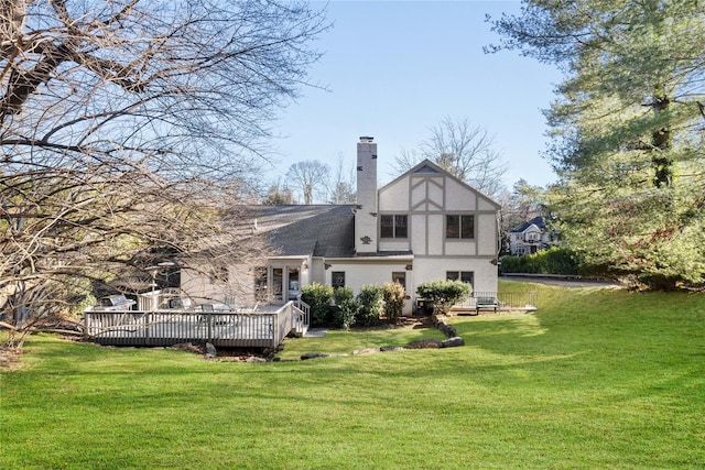 back of house with stucco siding, a chimney, a deck, and a yard