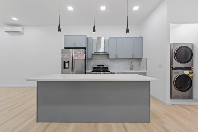 kitchen with wall chimney range hood, gray cabinets, stacked washing maching and dryer, appliances with stainless steel finishes, and decorative light fixtures