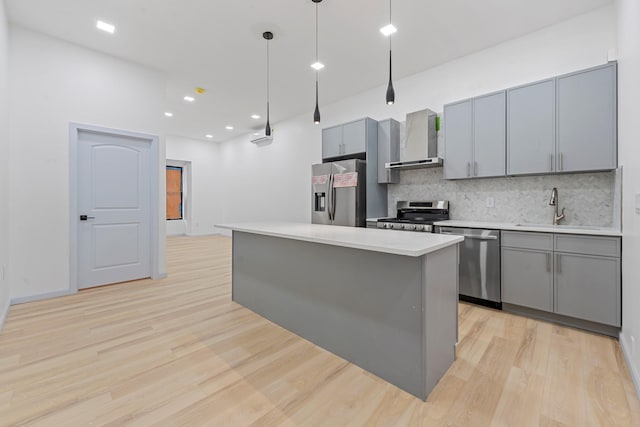 kitchen featuring a center island, wall chimney range hood, sink, decorative light fixtures, and stainless steel appliances