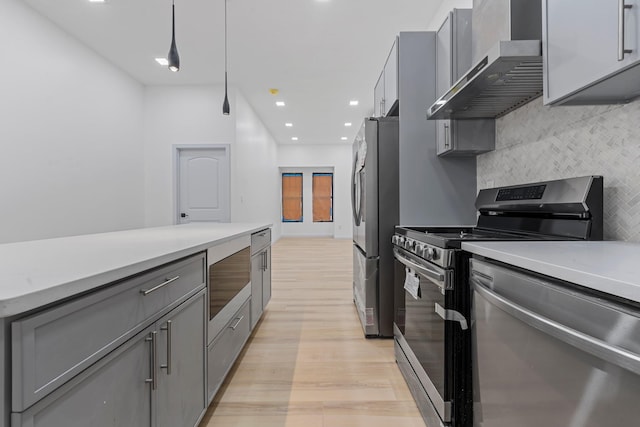 kitchen featuring stainless steel appliances, hanging light fixtures, gray cabinetry, and wall chimney range hood