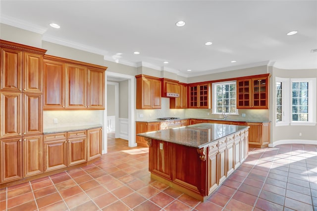 kitchen featuring light tile patterned flooring, stainless steel gas cooktop, ornamental molding, a kitchen island, and light stone countertops