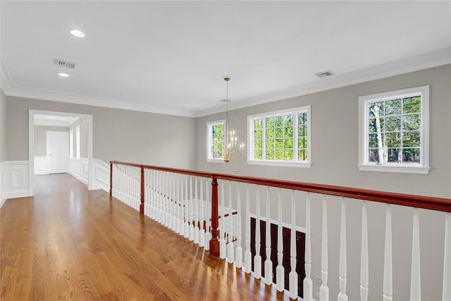 corridor with hardwood / wood-style flooring, ornamental molding, and a chandelier