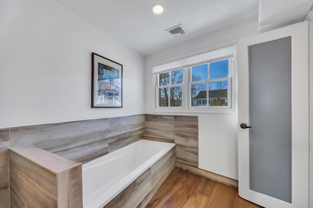 bathroom with tiled tub and hardwood / wood-style flooring