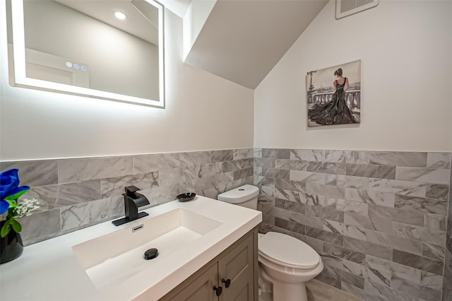 bathroom featuring toilet, vanity, tile walls, and lofted ceiling