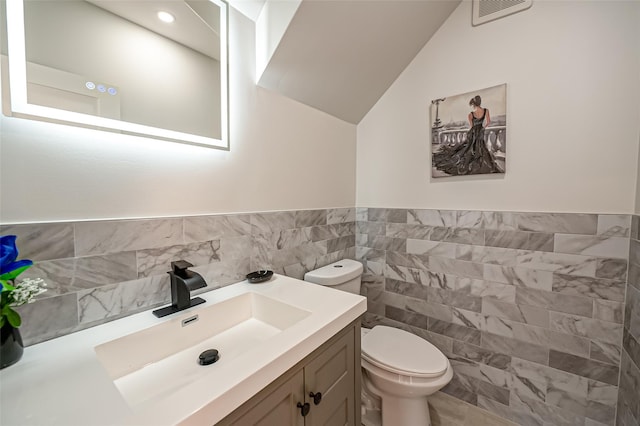 bathroom with tile walls, toilet, lofted ceiling, and vanity