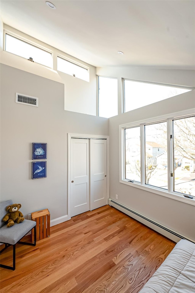 bedroom with a high ceiling, a baseboard radiator, a closet, and light hardwood / wood-style flooring