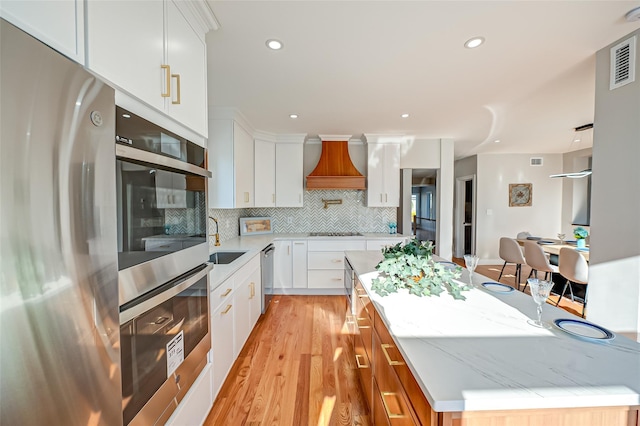 kitchen with premium range hood, a center island, decorative backsplash, white cabinets, and appliances with stainless steel finishes