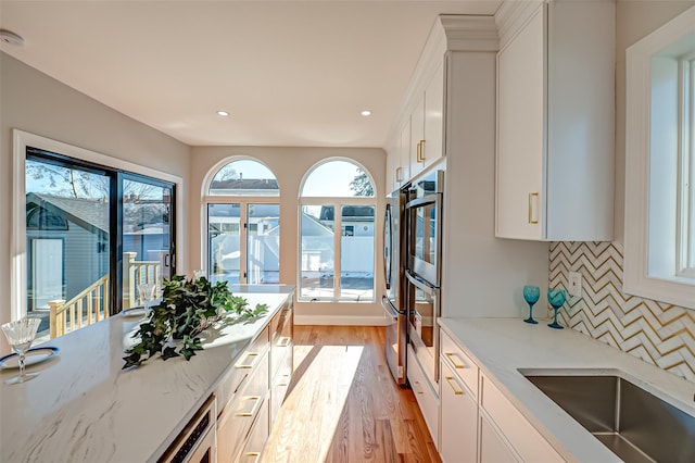 kitchen featuring decorative backsplash, white cabinetry, light hardwood / wood-style flooring, and light stone countertops