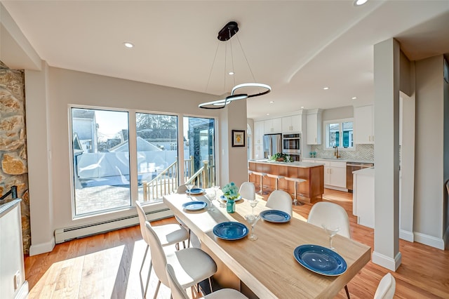 dining room with sink, light hardwood / wood-style flooring, plenty of natural light, and a baseboard heating unit