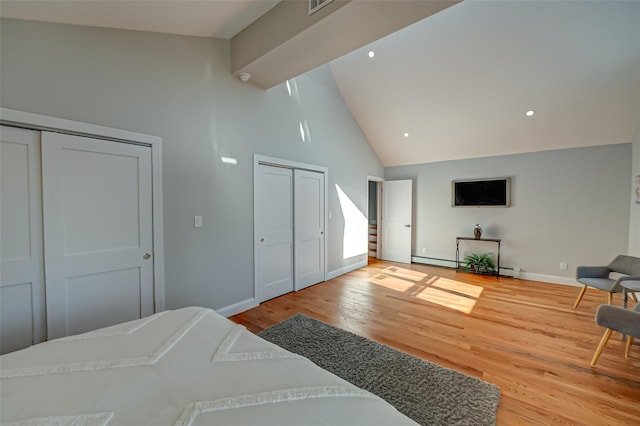 bedroom with two closets, light wood-type flooring, high vaulted ceiling, and a baseboard heating unit